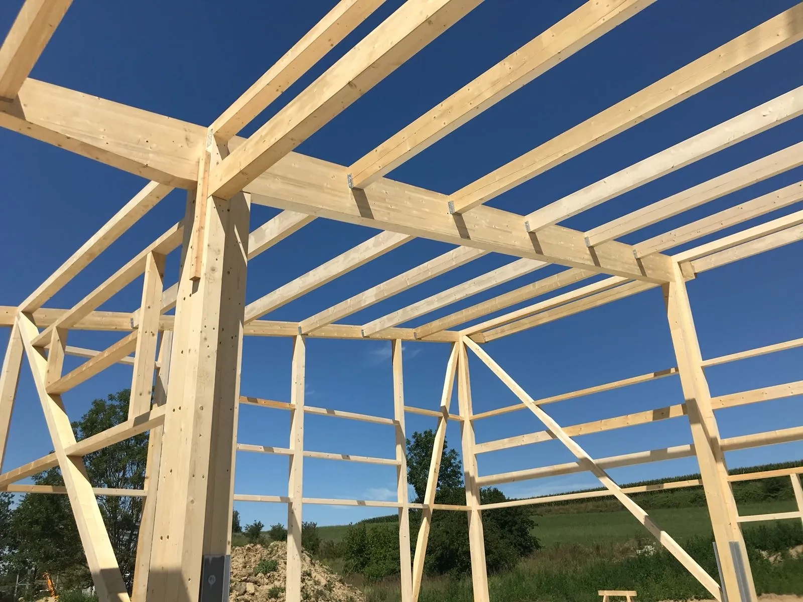 Tragwerk eines Holzrahmenbaus mit Stützen, Pfetten und Kopfbändern vor blauem Himmel