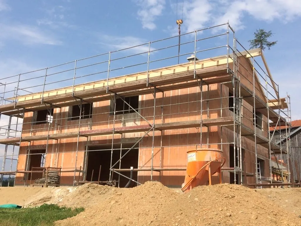 Rohbau eines zweigeschossigen Wohnhauses mit Gerüst und Betonkübel